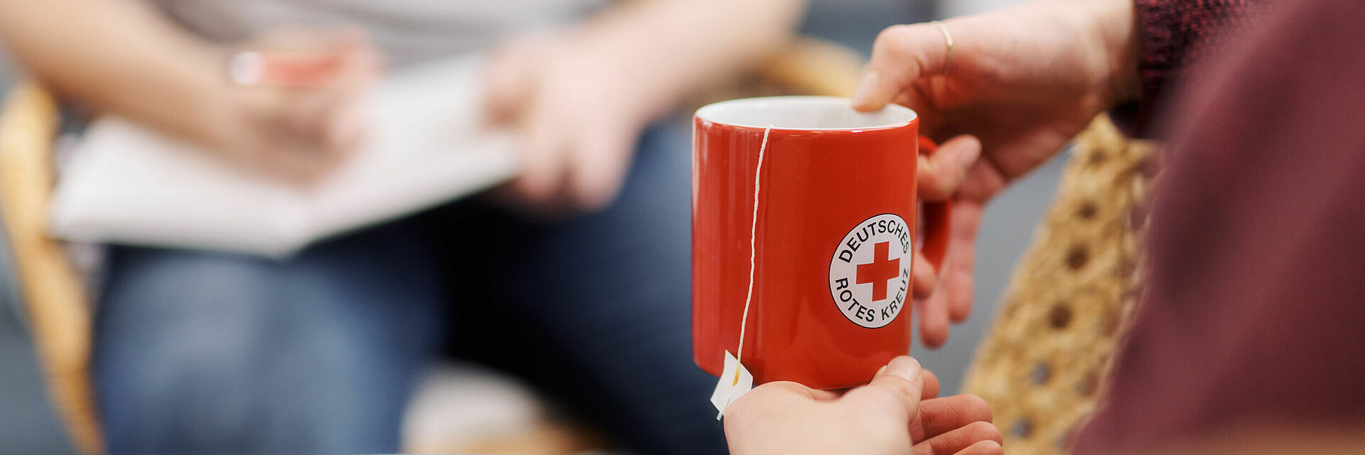 Person im Gruppengesprächskontext hält rote Teetasse