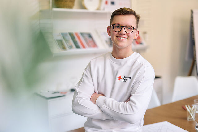 Symbolfoto junger Mitarbeiter des DRK, er trägt ein weißes Sweatshirt mit DRK