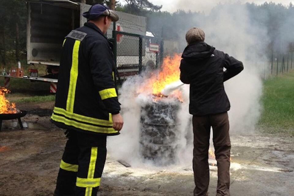 Ein Ausbilder beobachtet eine übende Person beim Feuer löschen.