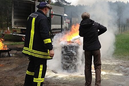 Ein Ausbilder beobachtet eine übende Person beim Feuer löschen.